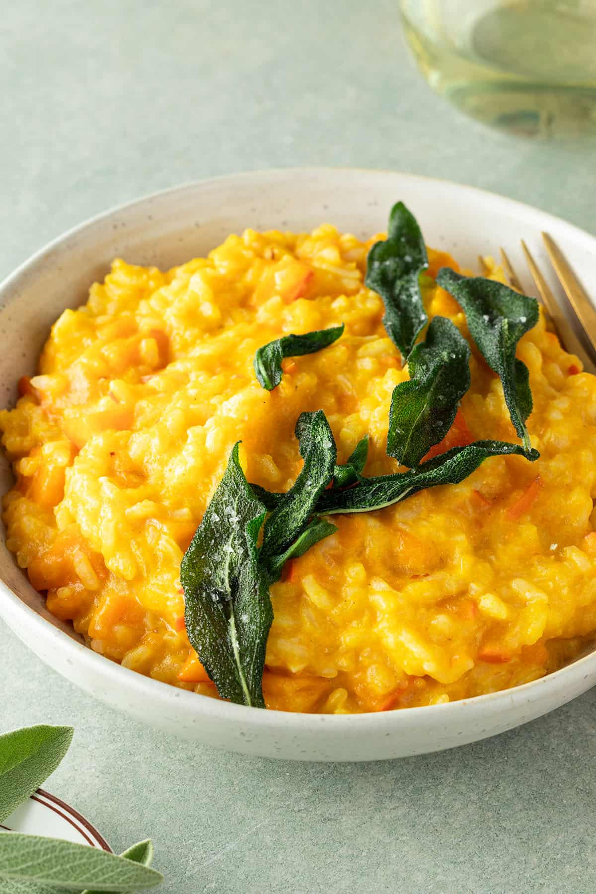 Teller mit cremigem K&uuml;rbisrisotto und mit knusprigen Salbei, Deko im Bildrand.