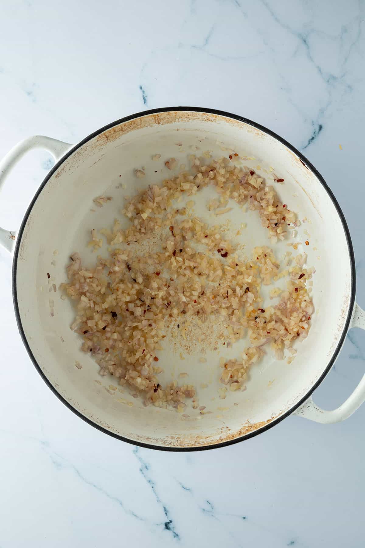 Schalotten und Knoblauch werden mit Chiliflocken in einem Topf angebraten.