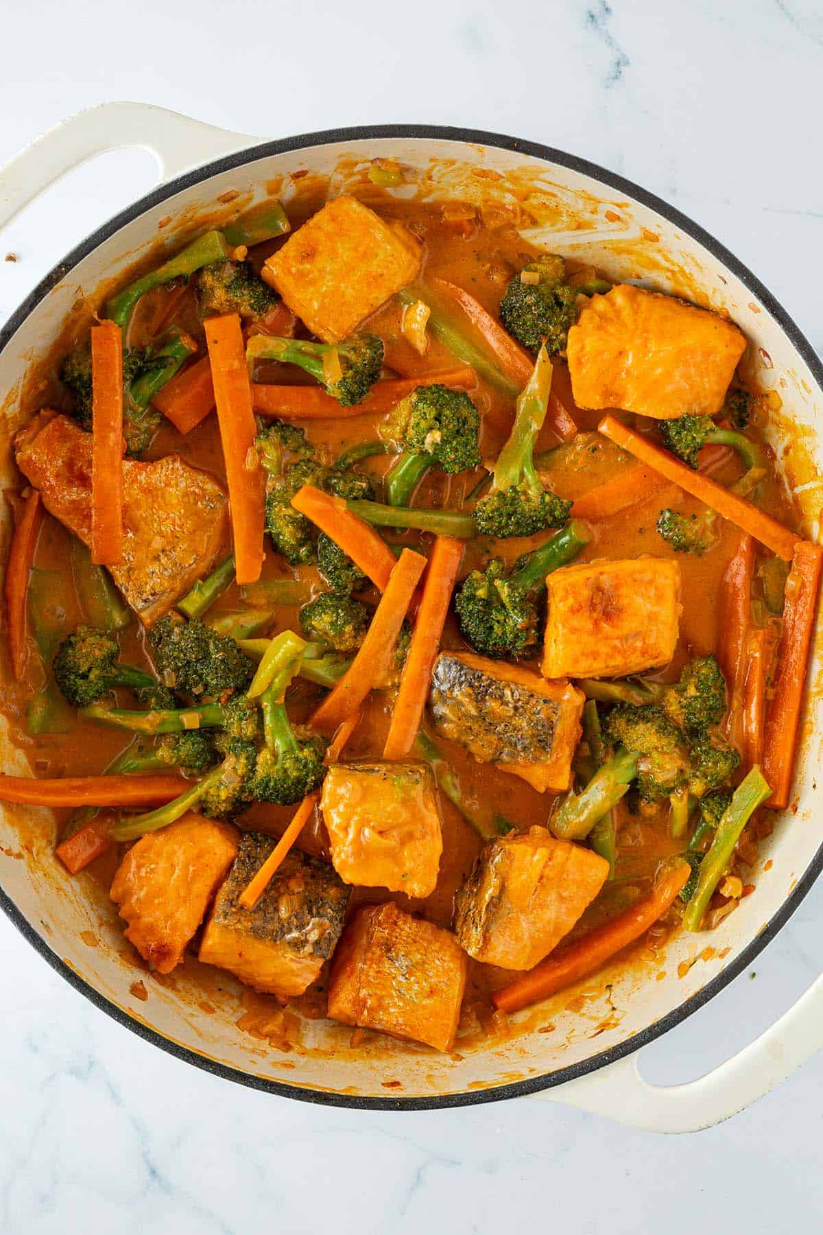 Fertig gegarte Lachsw&uuml;rfeln wurden unter die rote Thai Curry Sauce ger&uuml;hrt in der das Gem&uuml;se gekocht wurde.