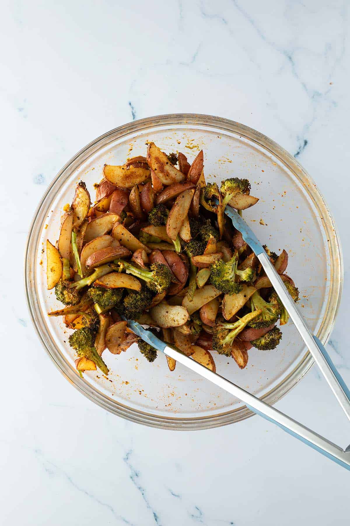 Ger&ouml;stete Kartoffelspalten und Brokkoli-R&ouml;schen wurden in einer Sch&uuml;ssel mit Gr&uuml;nem Pesto vermischt.