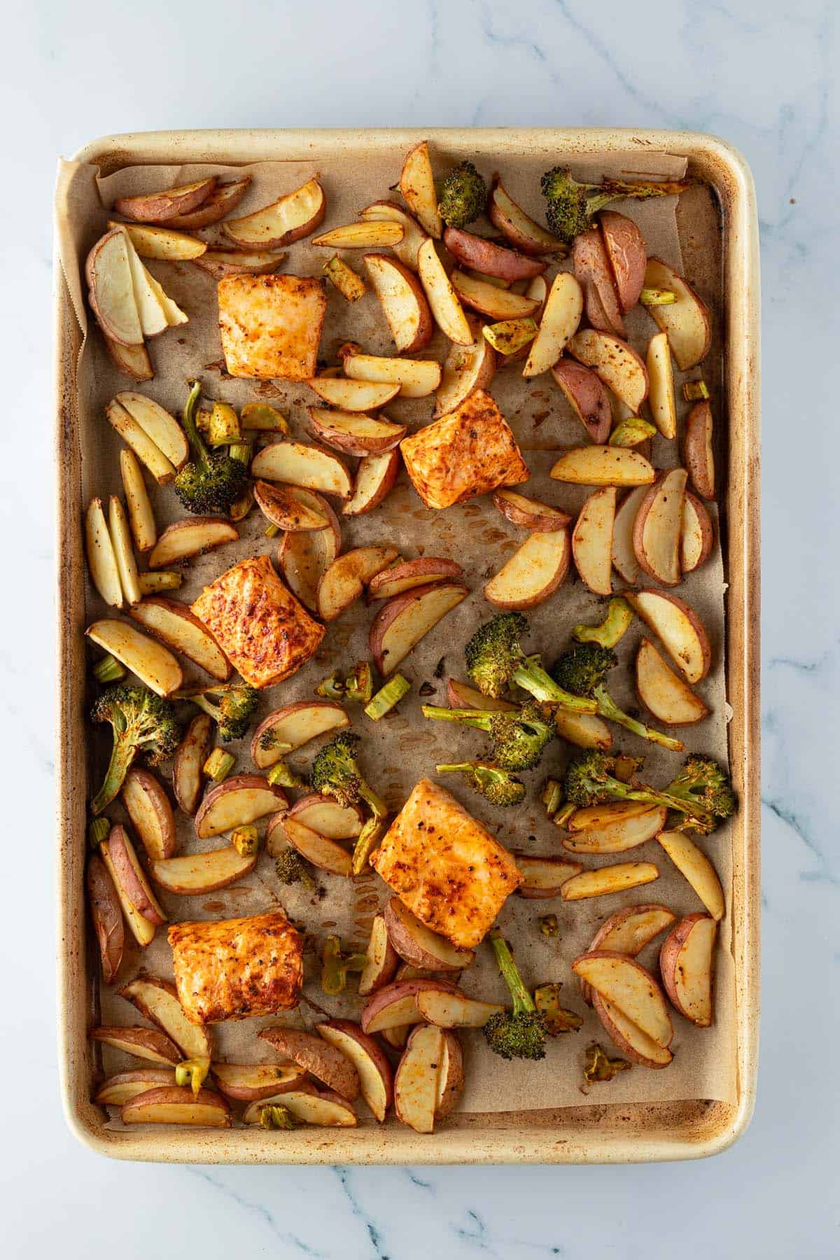 Ger&ouml;stete Kartoffeln, Lachsw&uuml;rfel und Brokkoli auf einem Blech.