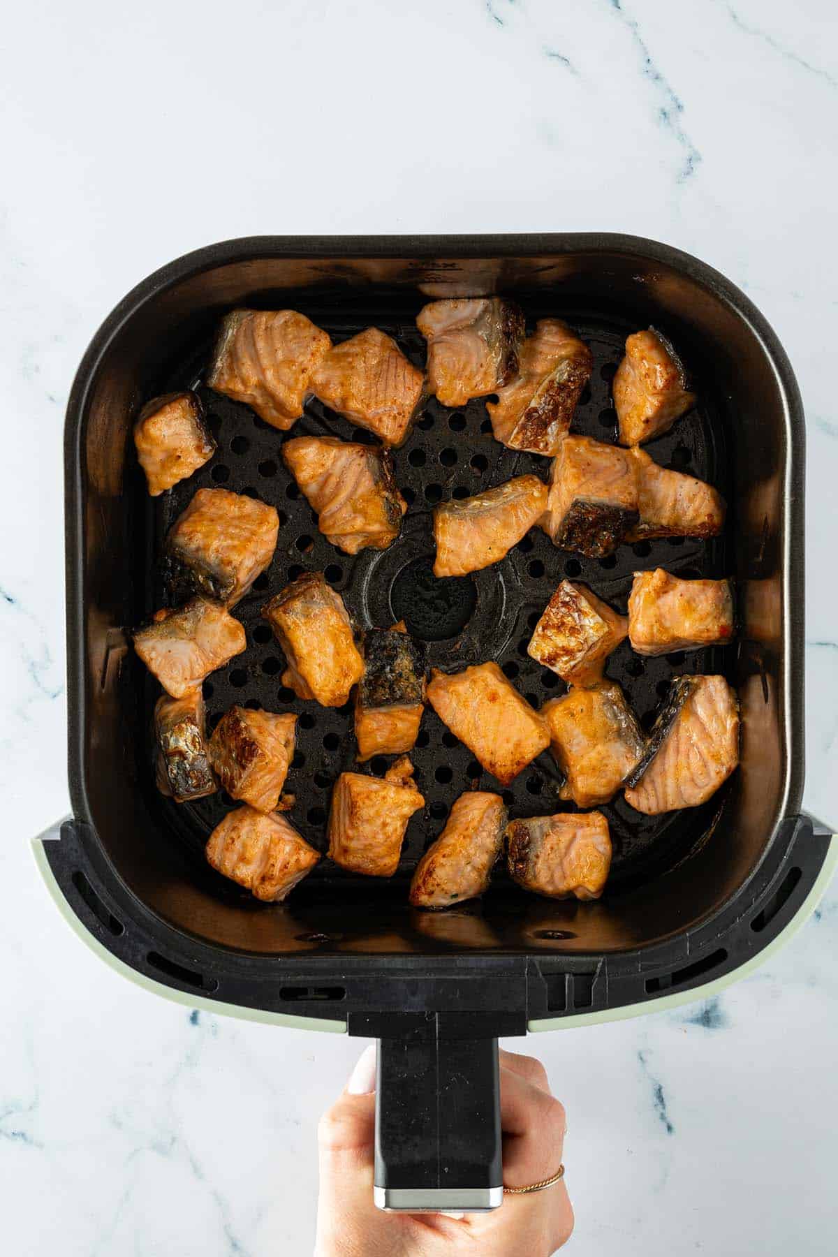 In kleine W&uuml;rfel geschnittene und mit einer Bang Bang Marinade gegarte Lachsfilets in einem Airfryer-Korb.
