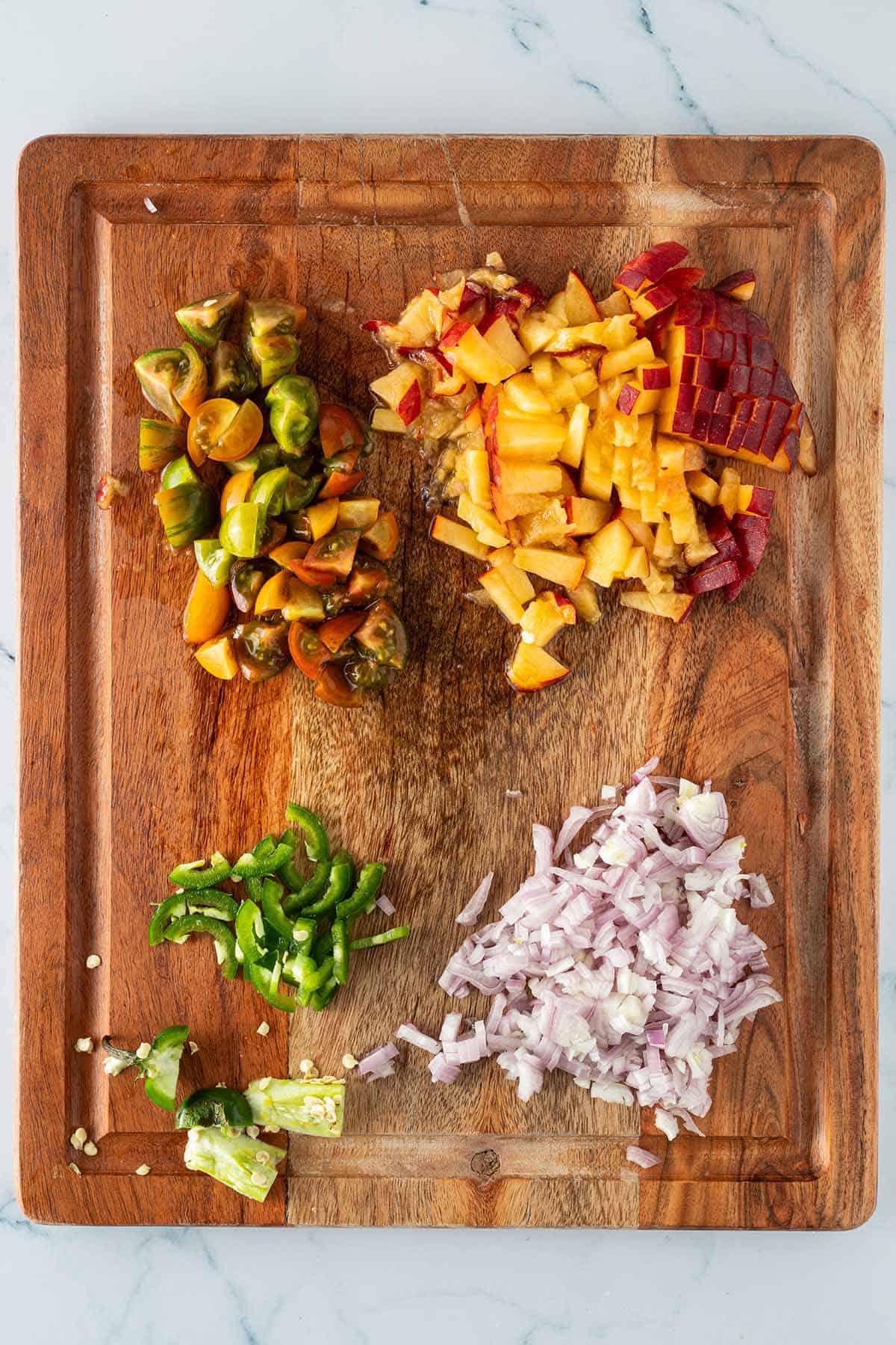 Fein gew&uuml;rfelte Pfirsiche, Tomaten, Schalotten und Jalape&ntilde;o auf einem Brett.