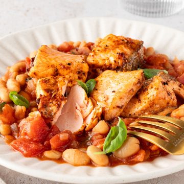 Saftig gegarte Lachsst&uuml;cke auf einer wei&szlig;en Bohnenpfanne mit Tomaten, Deko im Bildrand.