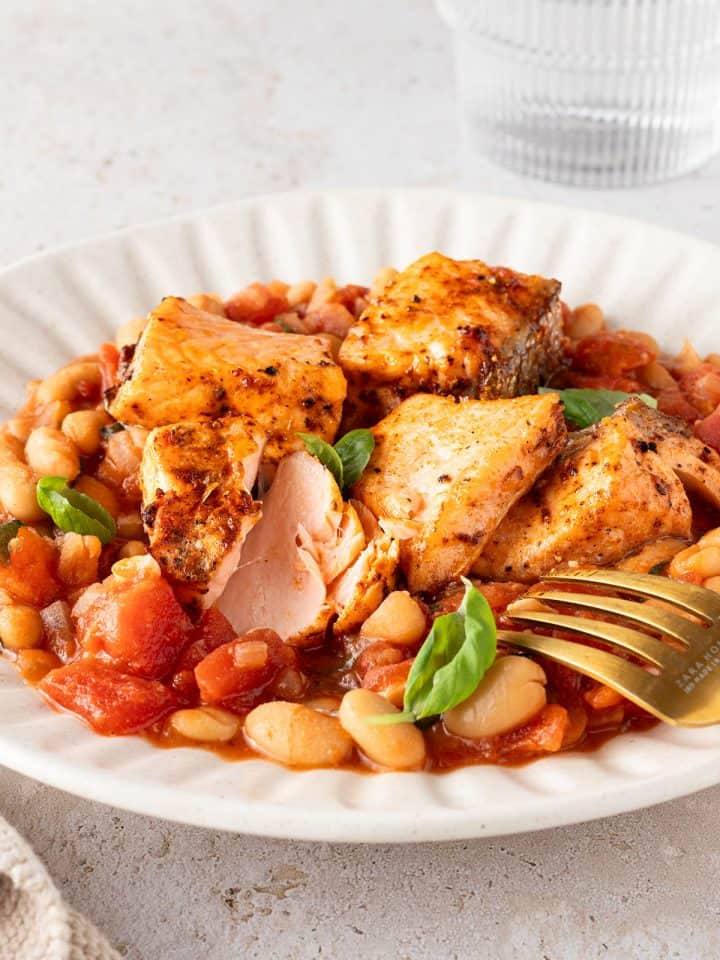 Saftig gegarte Lachsst&uuml;cke auf einer wei&szlig;en Bohnenpfanne mit Tomaten, Deko im Bildrand.