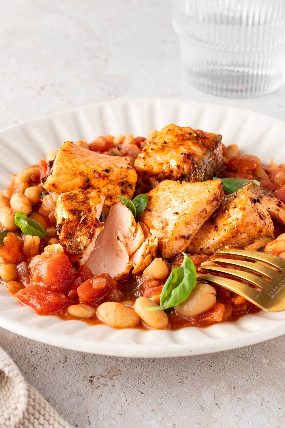 Saftig gegarte Lachsst&uuml;cke auf einer wei&szlig;en Bohnenpfanne mit Tomaten, Deko im Bildrand.