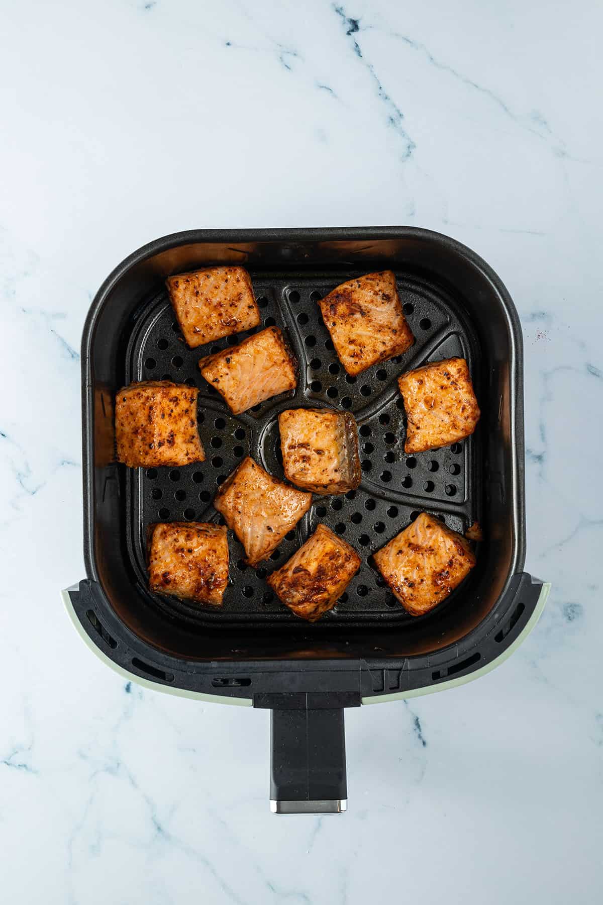Au&szlig;en knusprig gebackene Lachsst&uuml;cke in einem Airfryer-Korb.