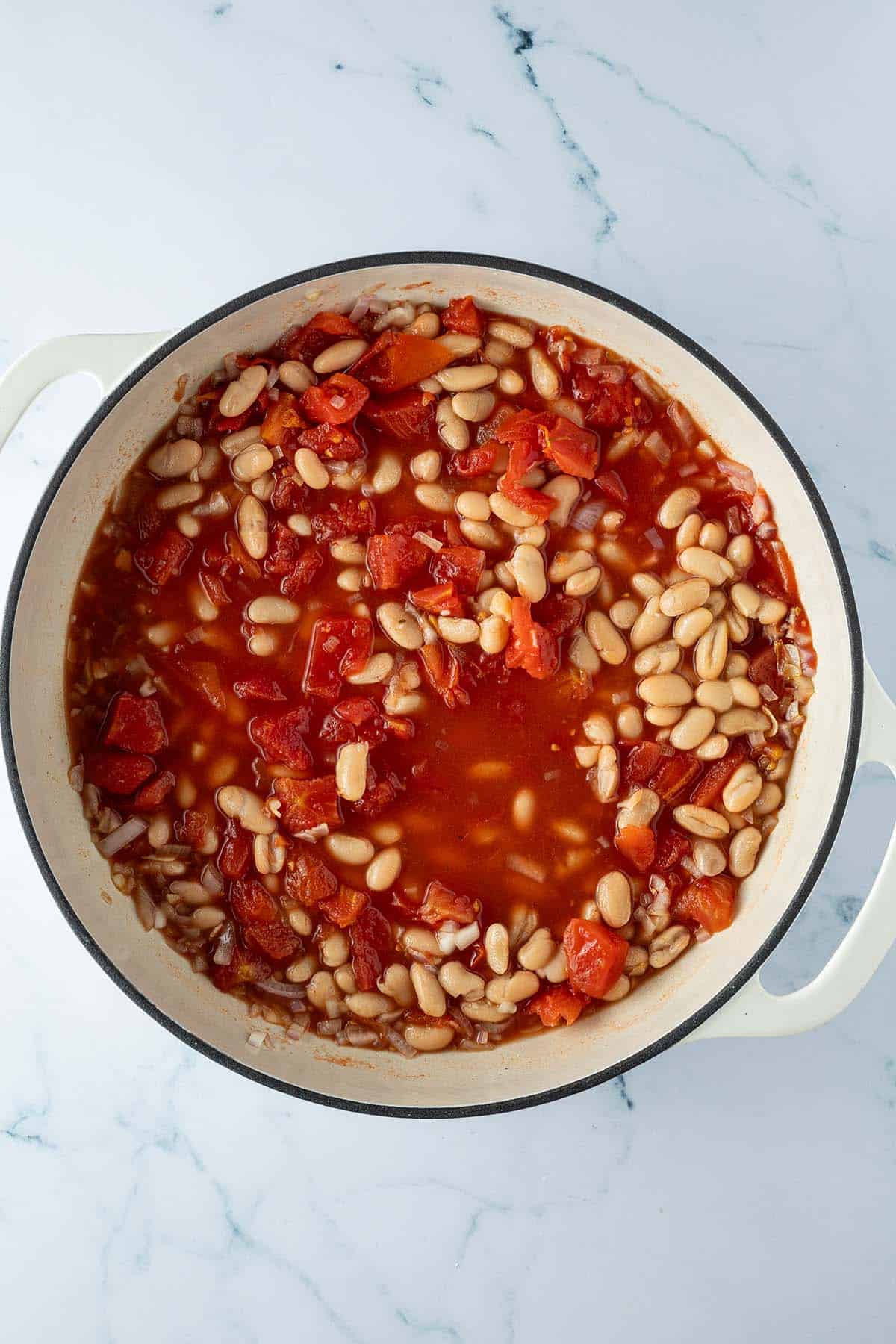 Wei&szlig;e Bohnen kochen in einer Pfanne mit Tomatensauce.
