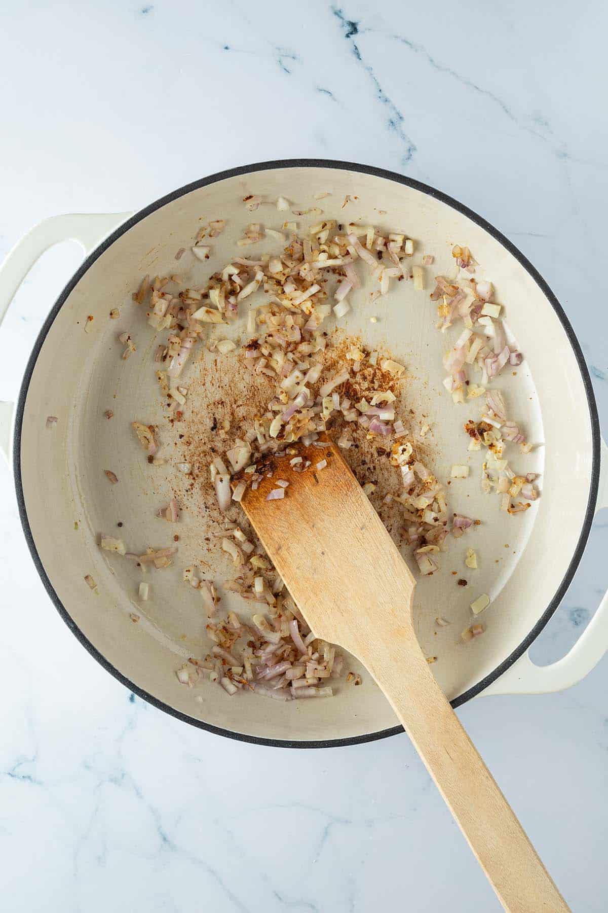 Schalottenw&uuml;rfel und Knoblauch werden in einer Pfanne glasig angebraten.
