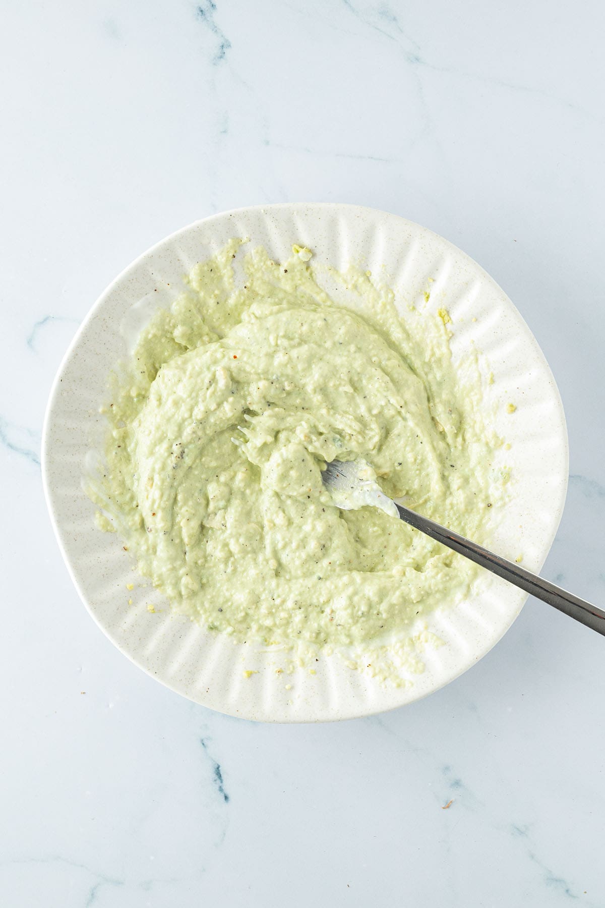 Cremiges, hellgr&uuml;nes Avocado-Joghurt-Dressing auf einem Teller mit einer Gabel.