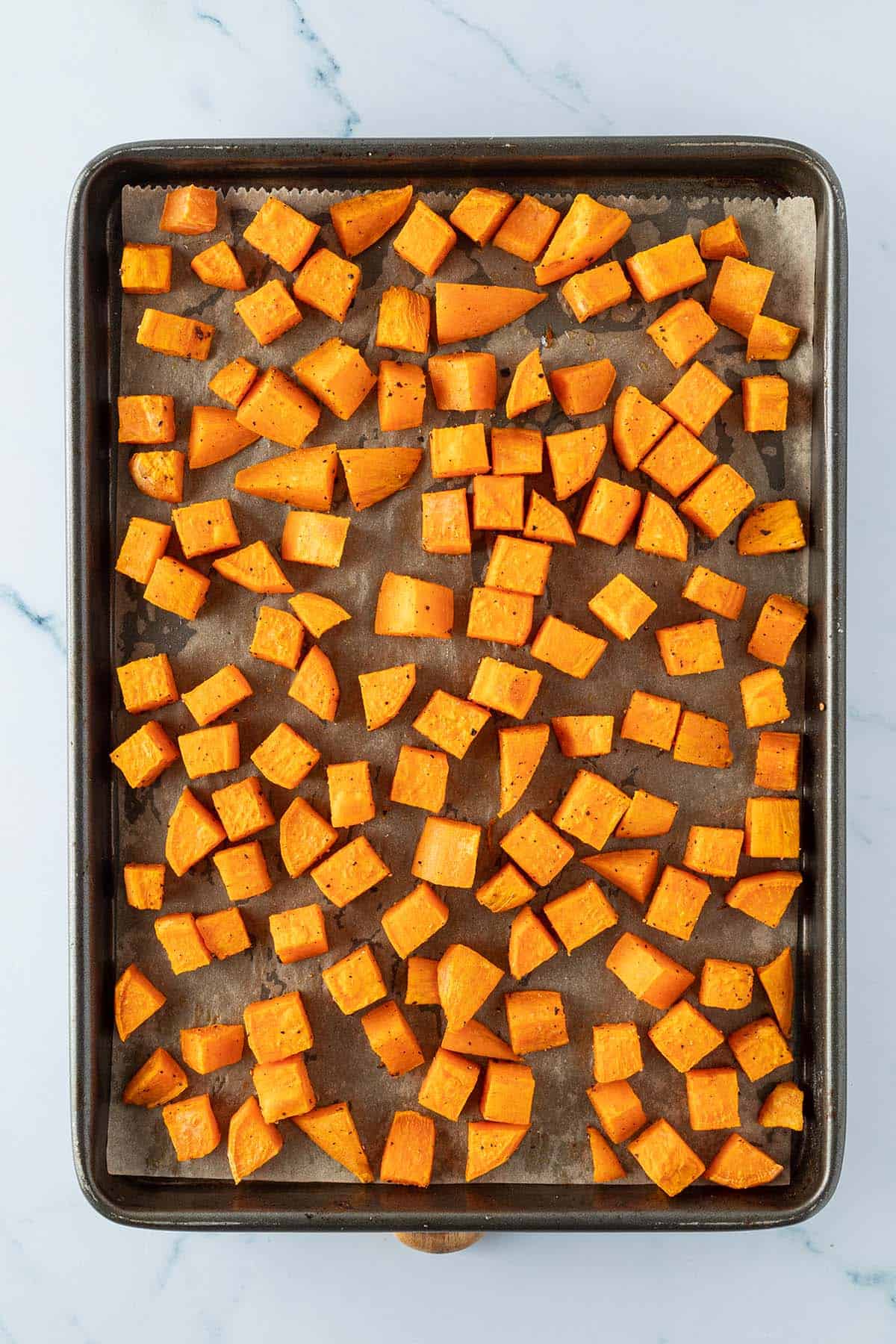 Ger&ouml;stete S&uuml;&szlig;kartoffel-W&uuml;rfel auf einem Blech mit Backpapier.