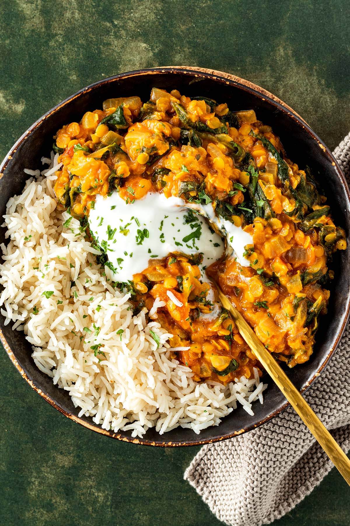 Eine Portion Linsen Dal mit Spinat, Reis und Joghurt in einer Sch&uuml;ssel auf gr&uuml;nem Untergrund.