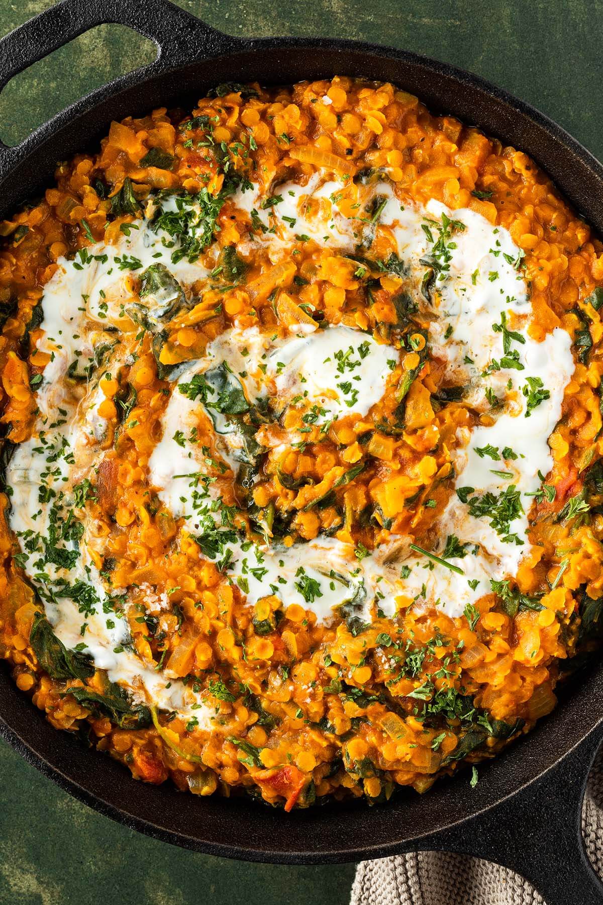 Nahaufnahme von einem Linsen Dal mit Spinat, da in einer Pfanne mit Joghurt und frischen Kr&auml;utern serviert wird.