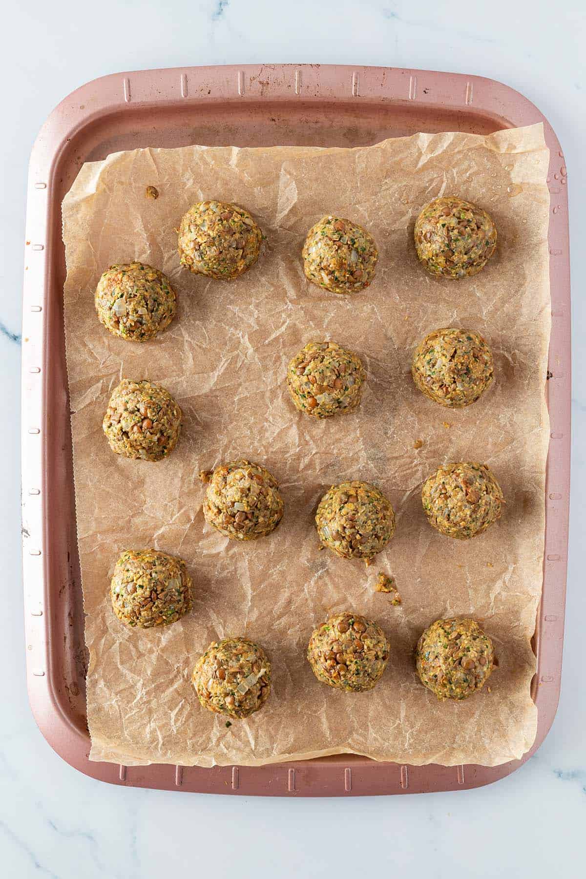 Zu runden Kugeln geformte Linsenb&auml;llchen auf einem Backblech.
