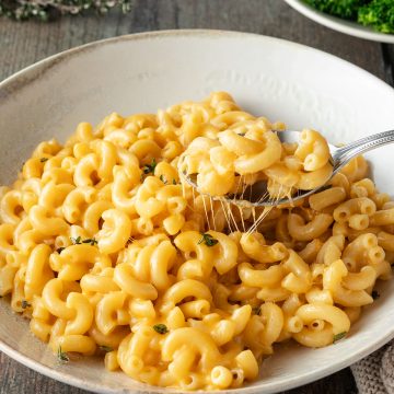 Ein Teller Mac and Cheese mit einem L&ouml;ffel, im Hintergrund ein Teller Brokkoli.