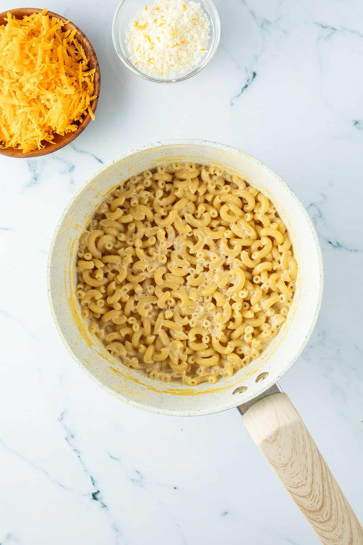 Macaroni in einem Topf, daneben zwei Schalen mit geriebenem K&auml;se.