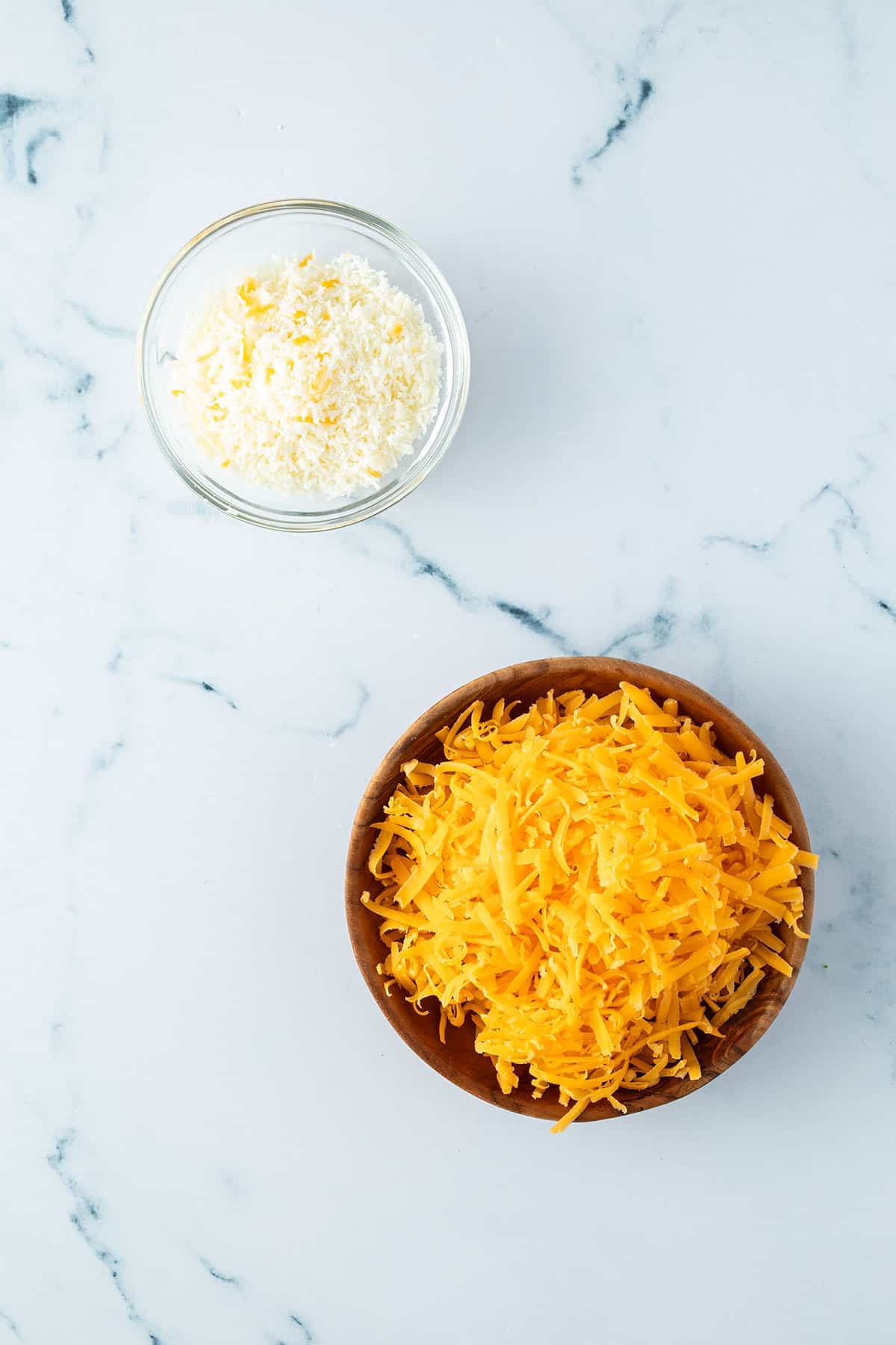 Eine Sch&uuml;ssel mit geriebenem Parmesan und eine Sch&uuml;ssel mit geriebenem Cheddar K&auml;se.
