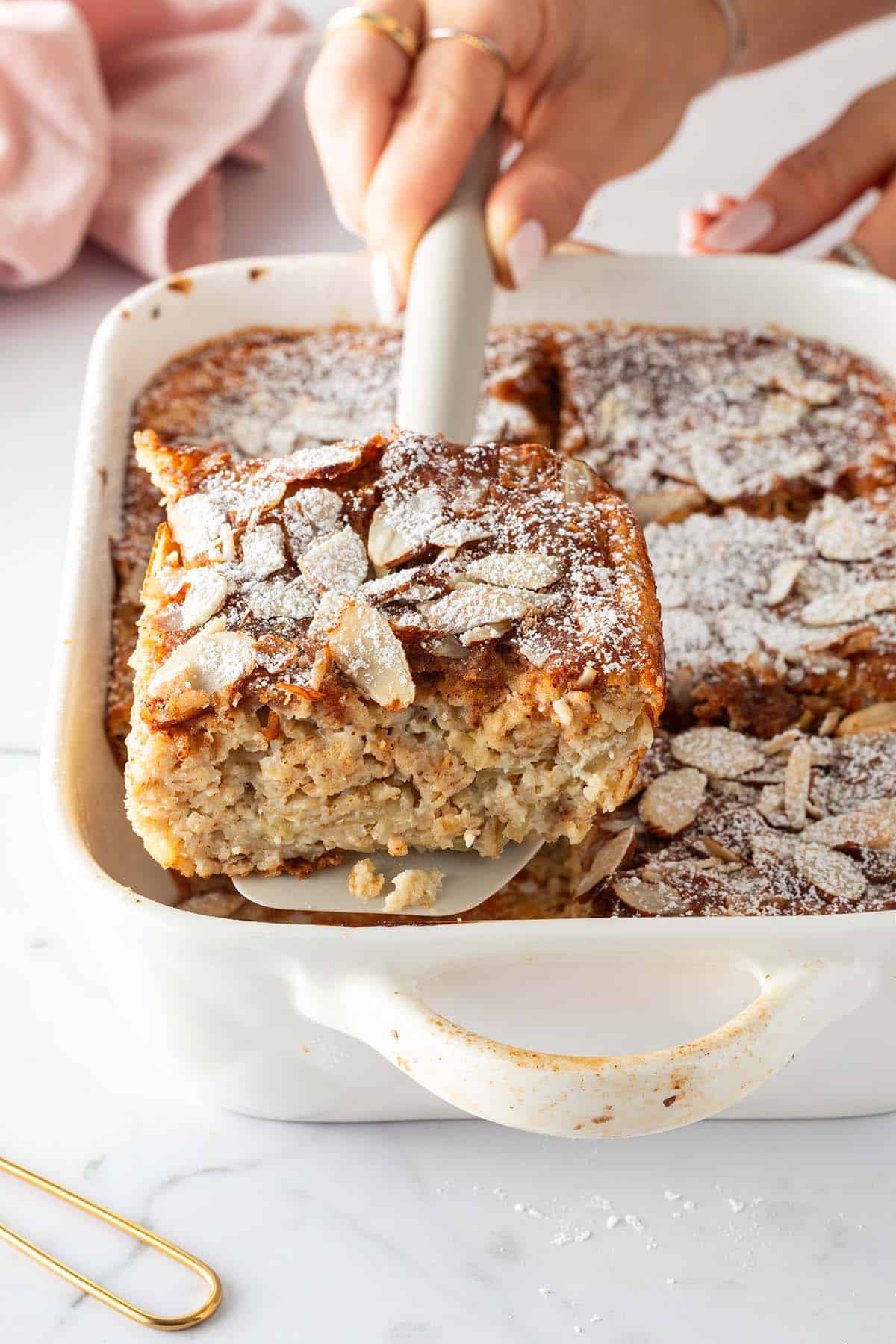 Eine Portion Mandel-Croissant Baked Oats wird mit einem Spatel aus einer Auflaufform gehoben.