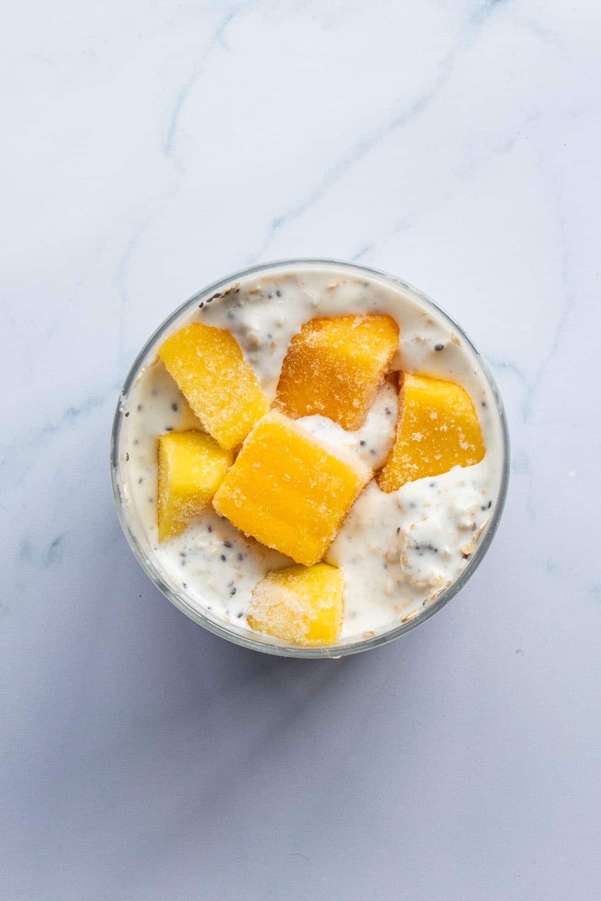 Fertig zubereitete Overnight Oats in einem Glas mit gefrorenen Mangost&uuml;ckchen.