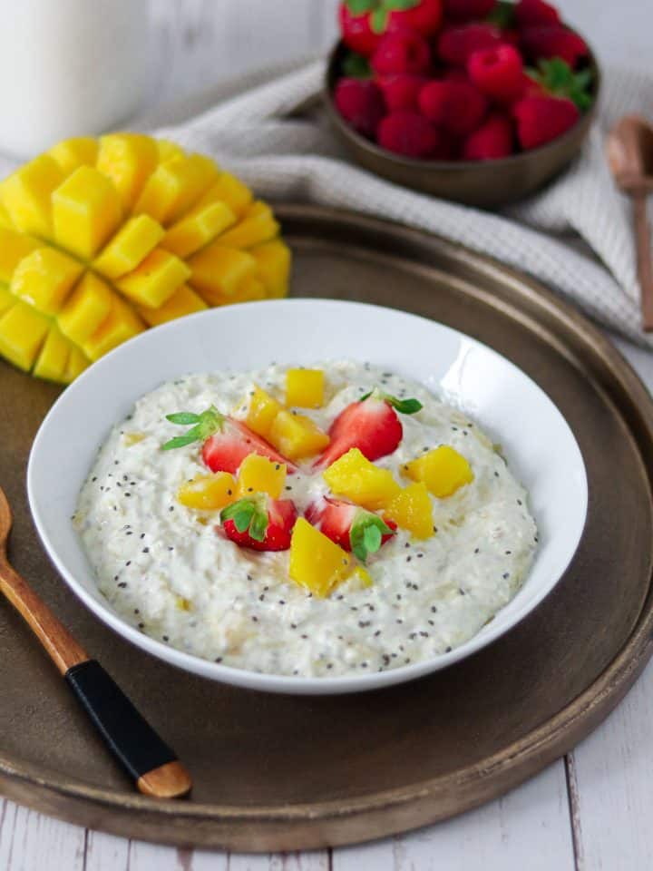 Eine Sch&uuml;ssel Overnight Oats mit Mango und Erdbeeren, Deko im Hintergrund.