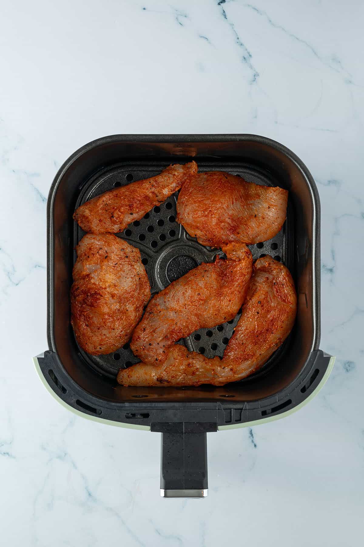 Marinierte H&auml;hnchenst&uuml;cke in einem Airfryer-Korb.