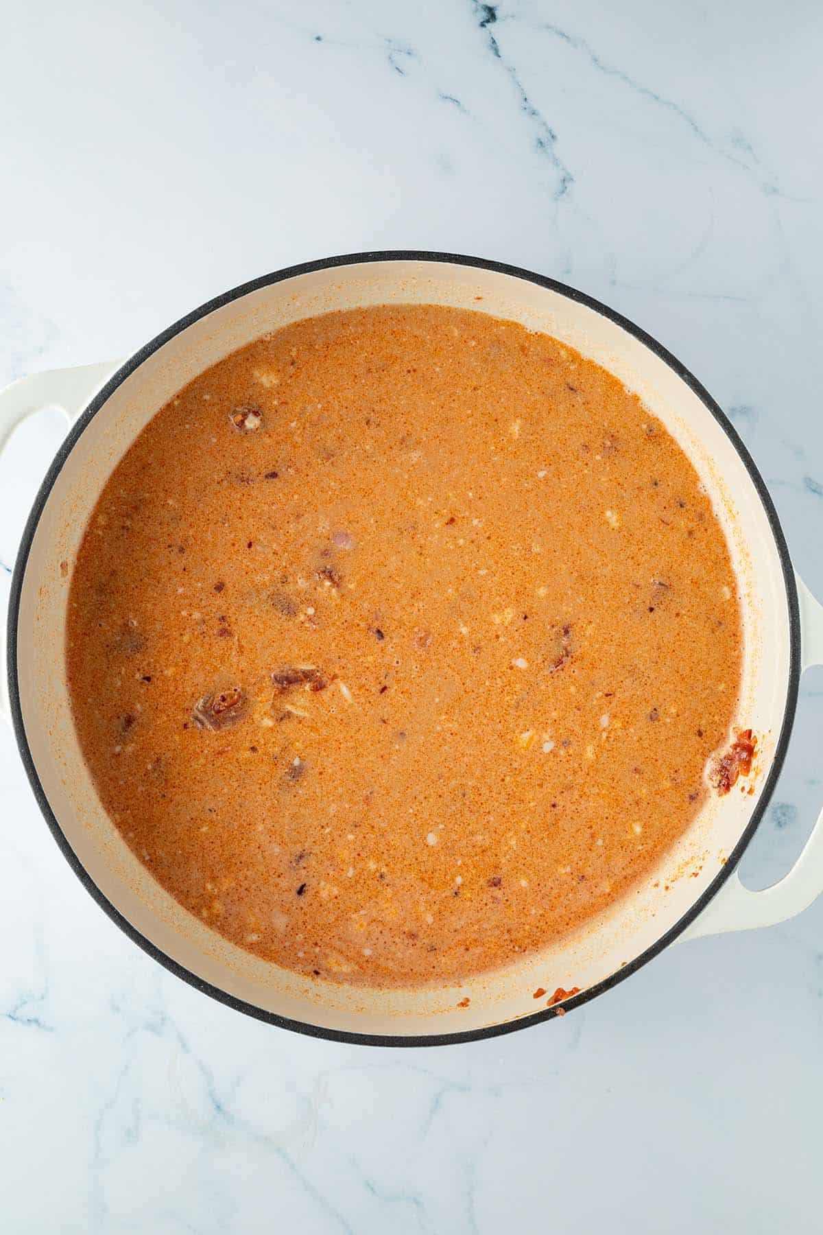 Fl&uuml;ssige Tomatensauce in einer Pfanne mit rohen Orzo-Nudeln.