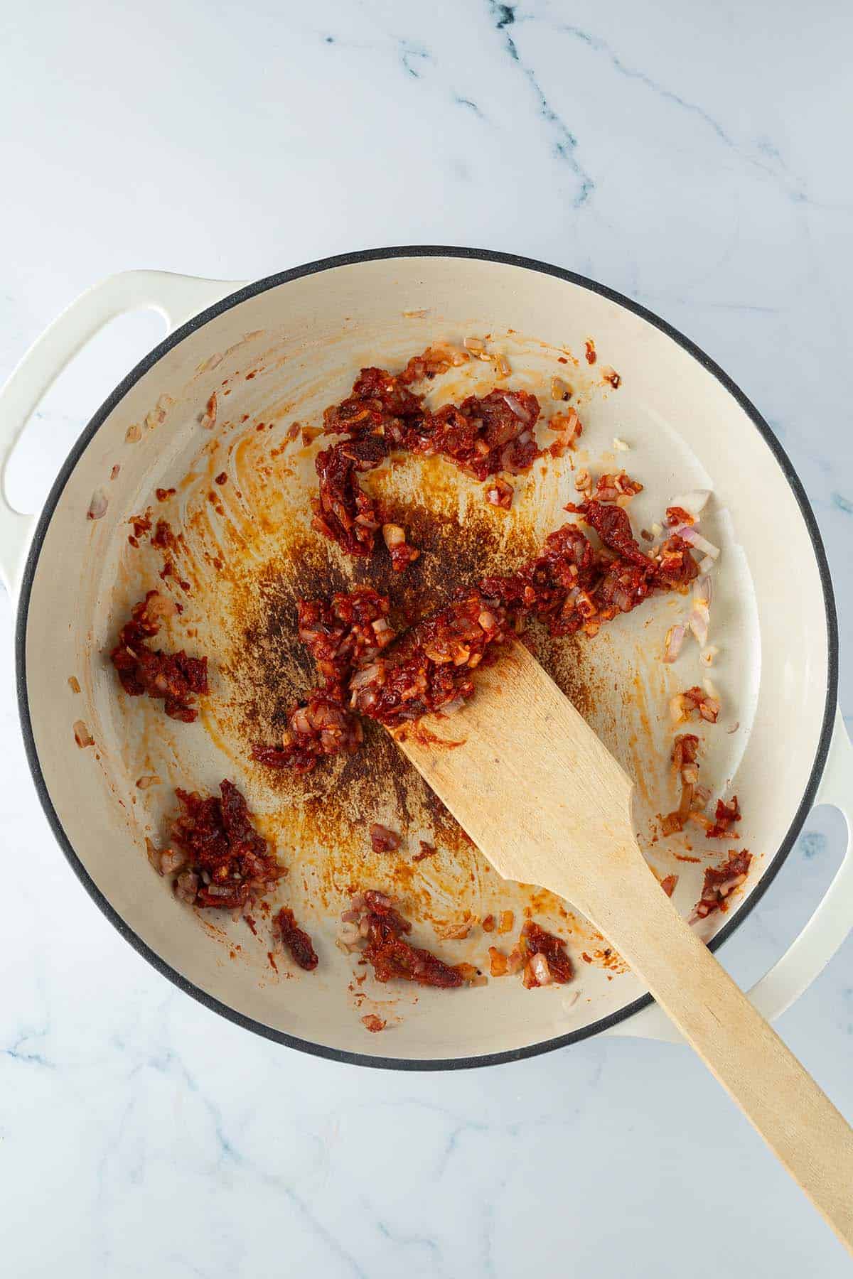 Zwiebeln, Knoblauch, getrocknete Tomaten und Tomatenmark werden in einer Pfanne angebraten.