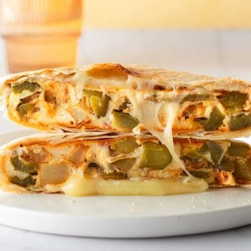 Halbiertes meal prep Fr&uuml;hst&uuml;cksandwich aufeinandergestapelt, gef&uuml;llt mit geschmolzenem K&auml;se und einem Omelett mit Paprika und Kartoffeln.