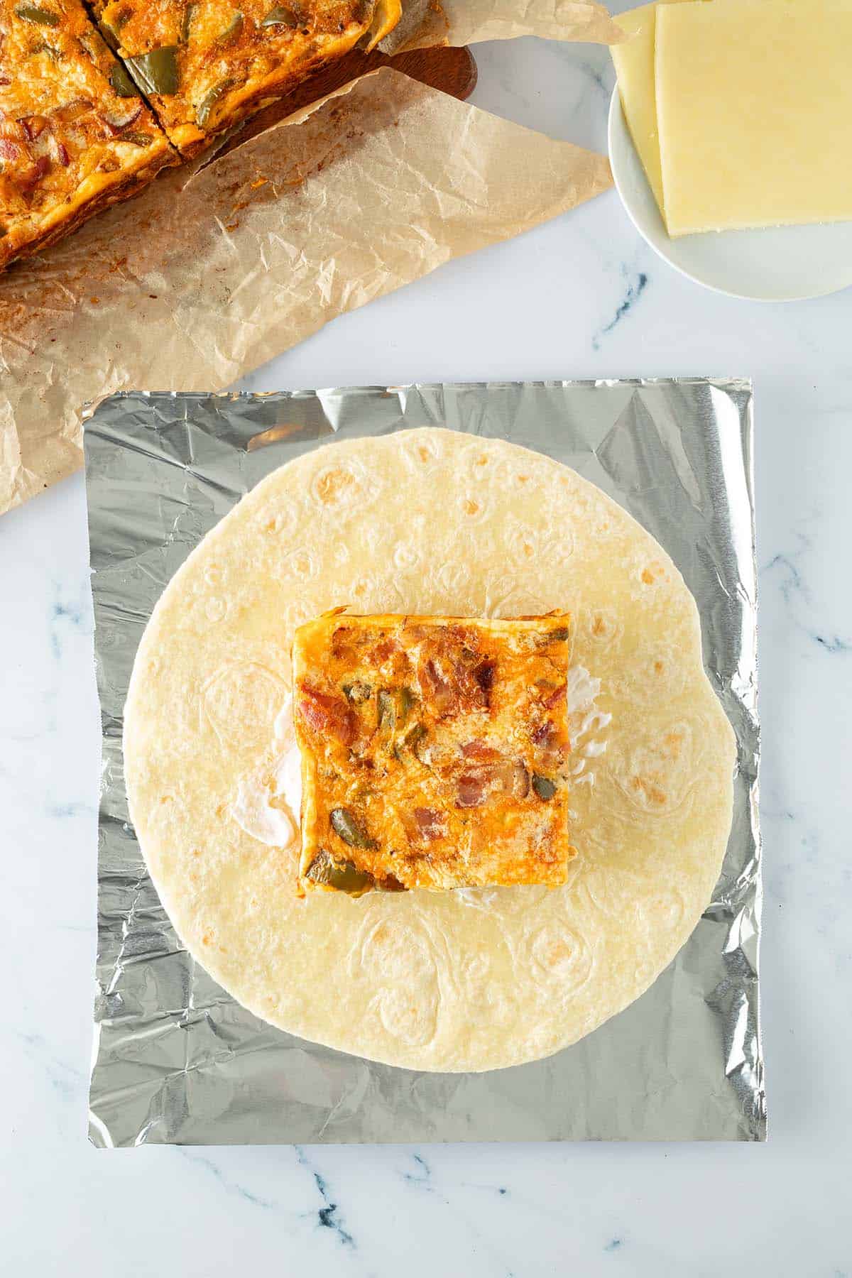 Tortilla auf Alufolie, belegt mit einem quadratischen St&uuml;ck Ofen-Omelett mit Paprika und Speck, K&auml;se und Schmand.