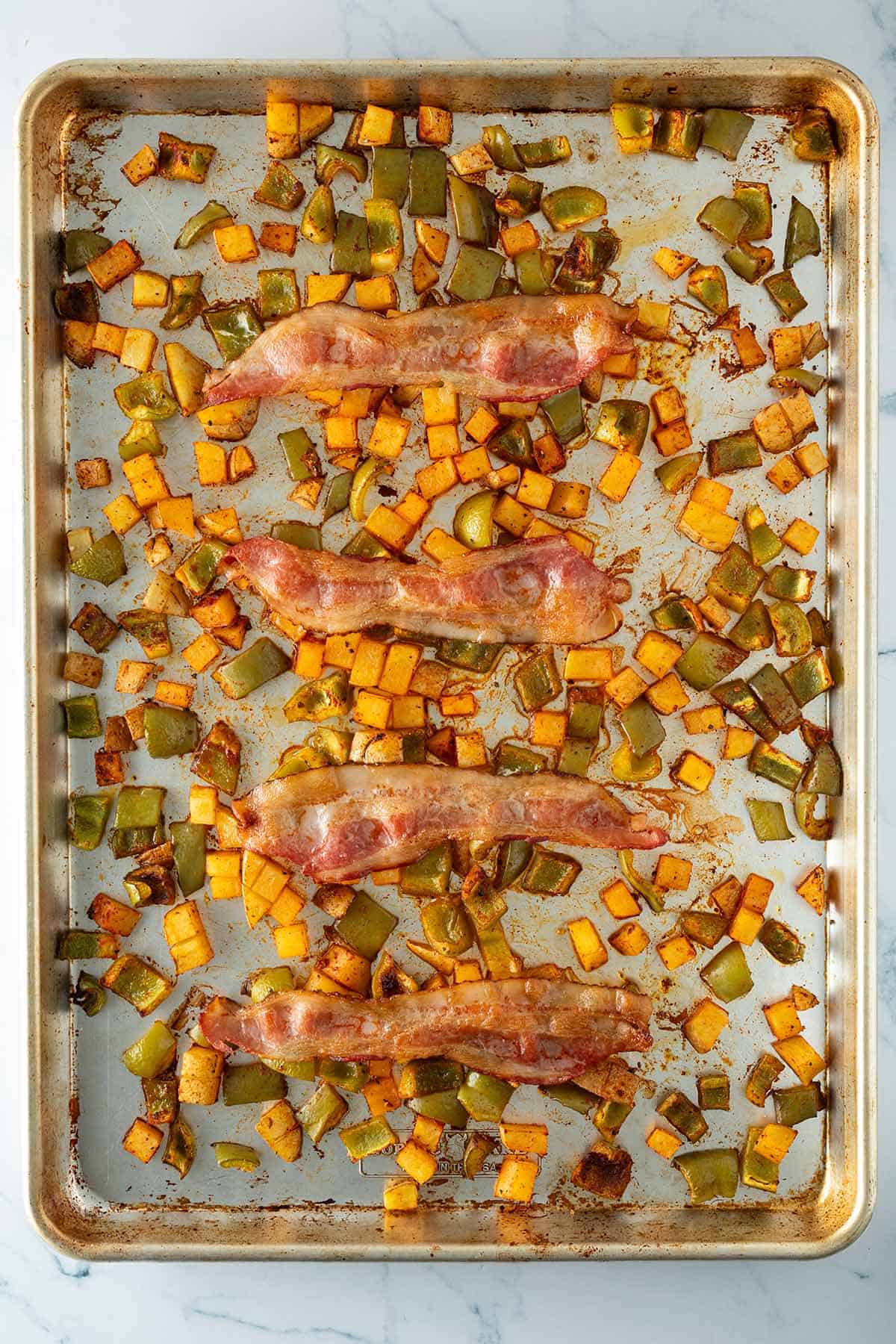 Ger&ouml;stete Paprika, Kartoffeln und 4 knusprige Speckstreifen auf einem Blech.