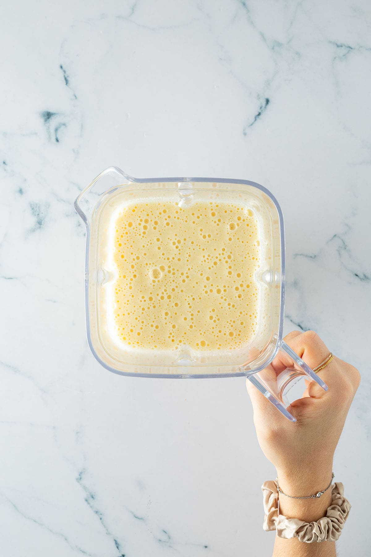 Hand h&auml;lt einen Mixerbeh&auml;lter mit p&uuml;rierter Eiermischung f&uuml;r die meal prep Fr&uuml;hst&uuml;ckssandwiches.