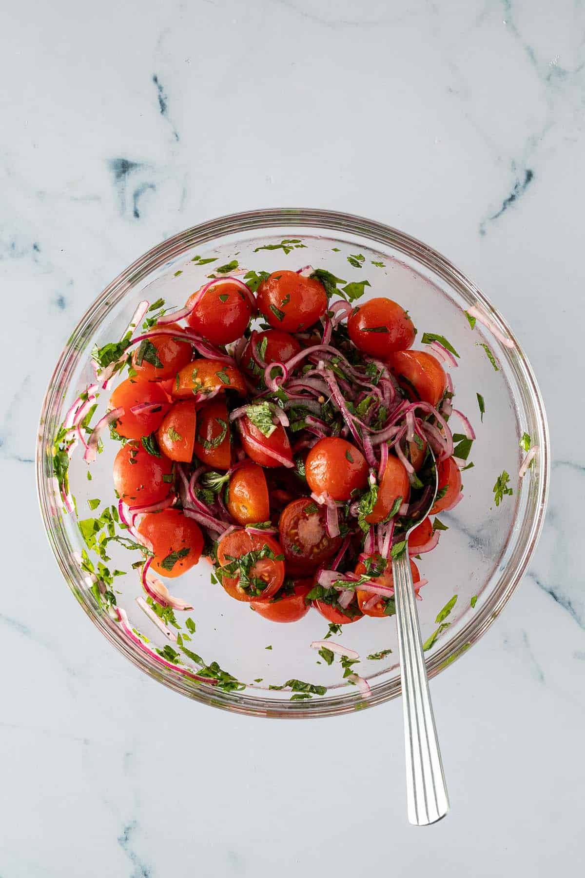 Tomatensalat mit halbierten Cherrytomaten, marinierten roten Zwiebeln und frischen Kr&auml;utern in einer Glassch&uuml;ssel.