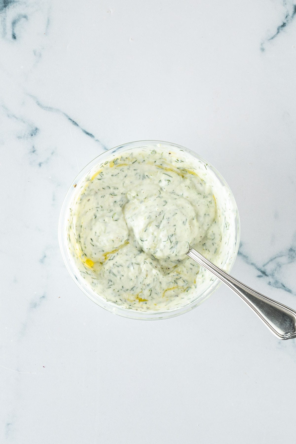 Cremiger Tzatziki mit geriebener Gurke und Dill in einer kleinen Glassch&uuml;ssel.