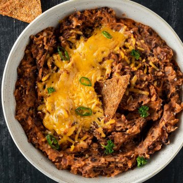 Mexikanisches Bohnenmus aus schwarzen Bohnen in einer Sch&uuml;ssel mit geschmolzenem K&auml;se on Top und Chips dazu.