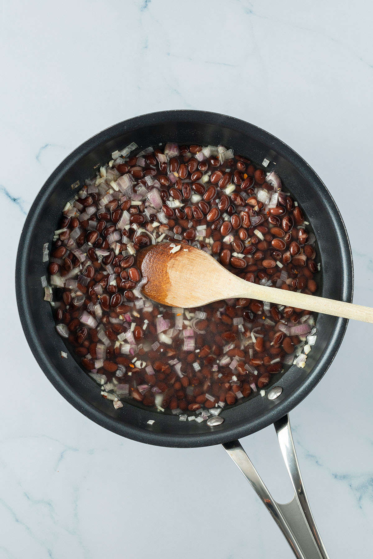 Eine Pfanne mit Schalotten-, Knoblauchw&uuml;rfeln, schwarzen Bohnen und Wasser.