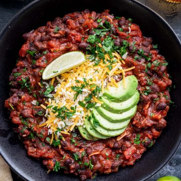 Mexikanische Bohnenpfanne mit Avocado, K&auml;se und Petersilie getappt in einem Teller, Deko im Bildrand.
