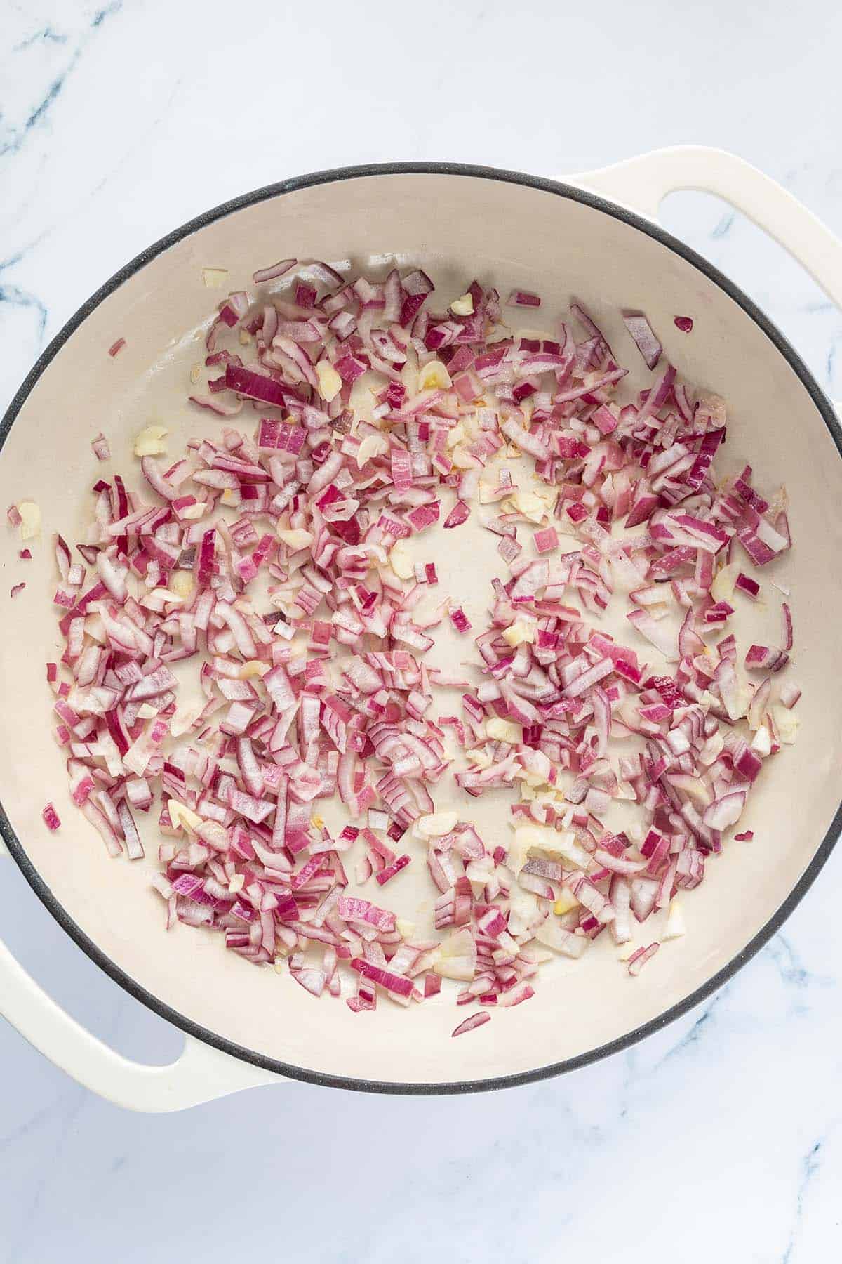 Kleingew&uuml;rfelte, rote Zwiebeln und Knoblauch werden in einer Pfanne angebraten.
