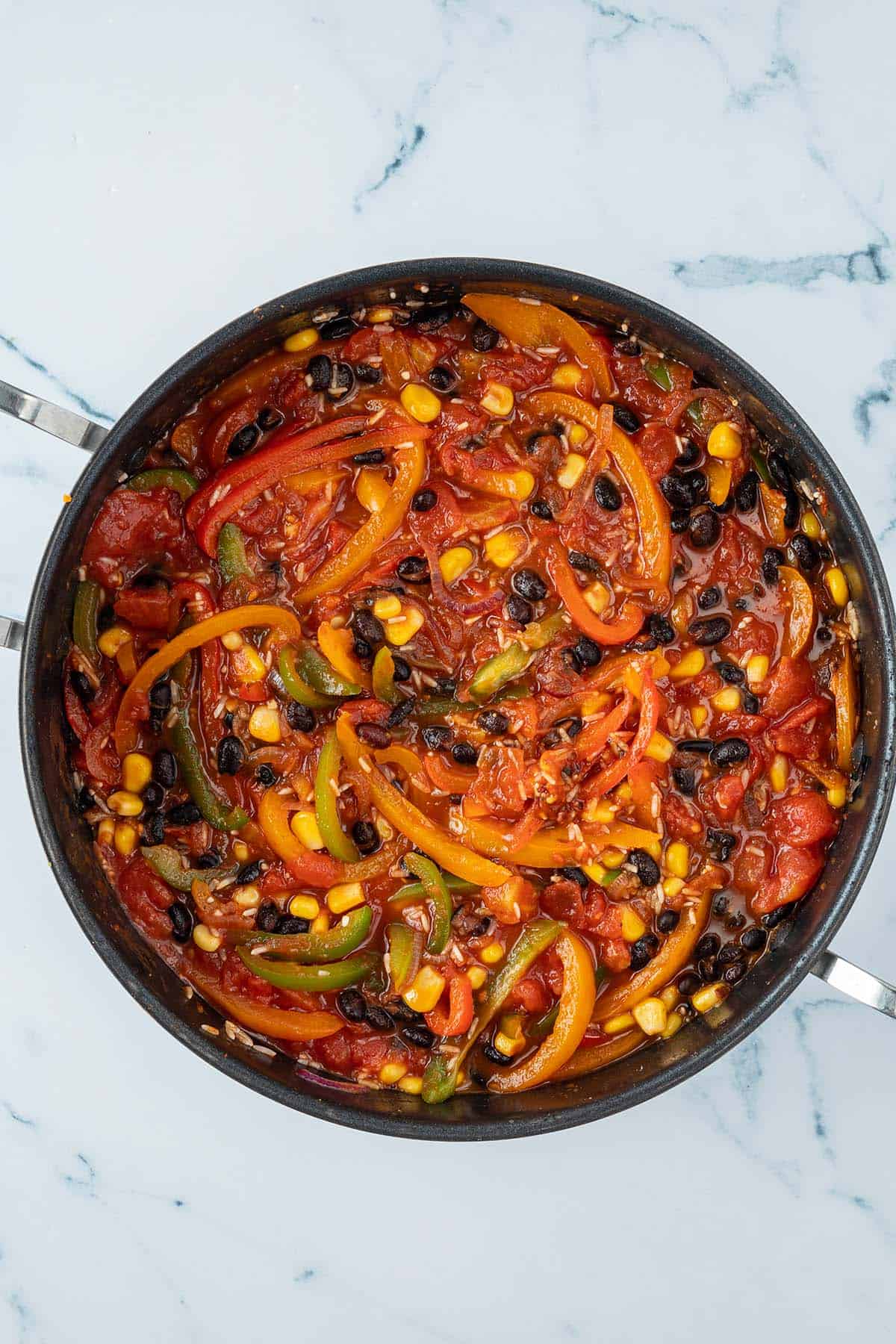 Angebratene Paprikastreifen mit ungekochtem Reis in einer Tomatensauce mit Bohnen und Mais.