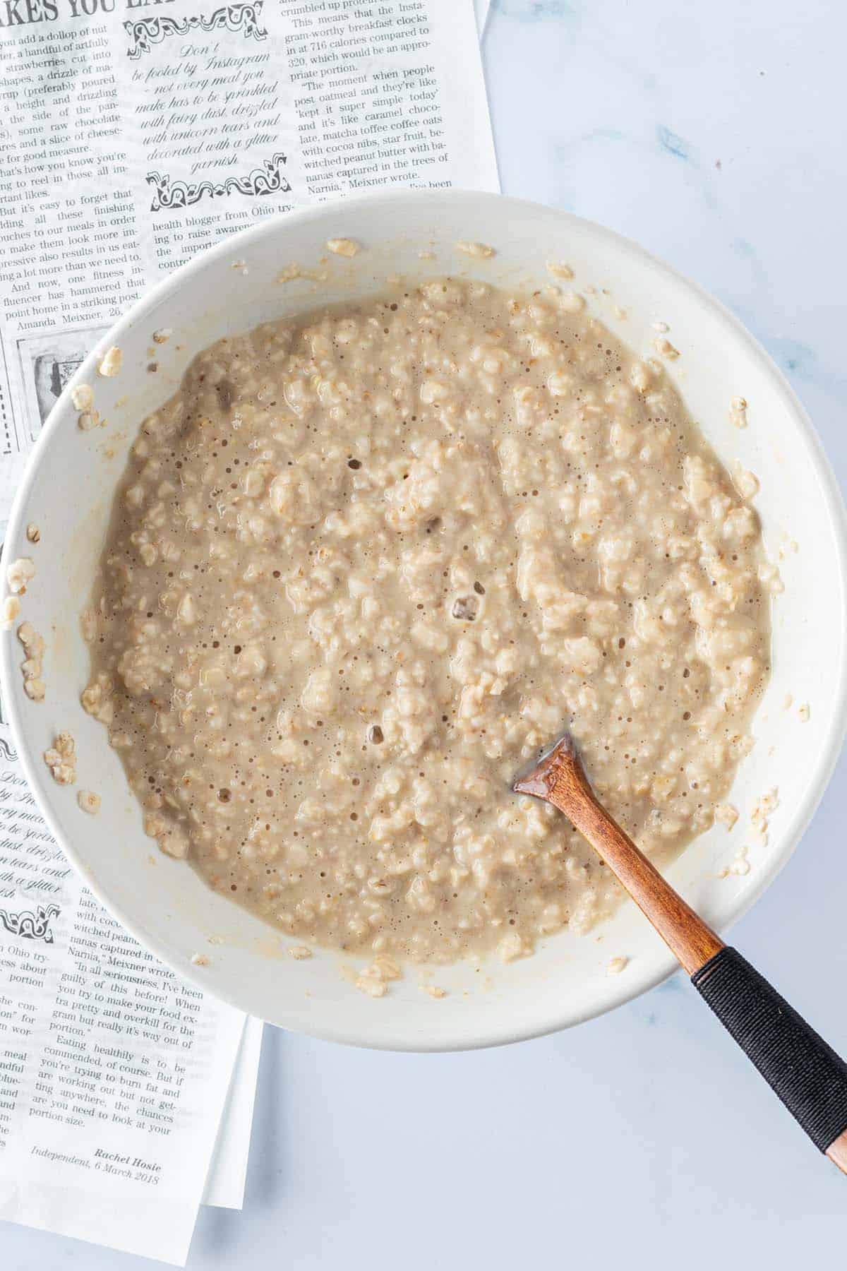 Cremiges Mikrowellen Porridge in einer Sch&uuml;ssel mit einem Holzl&ouml;ffel.