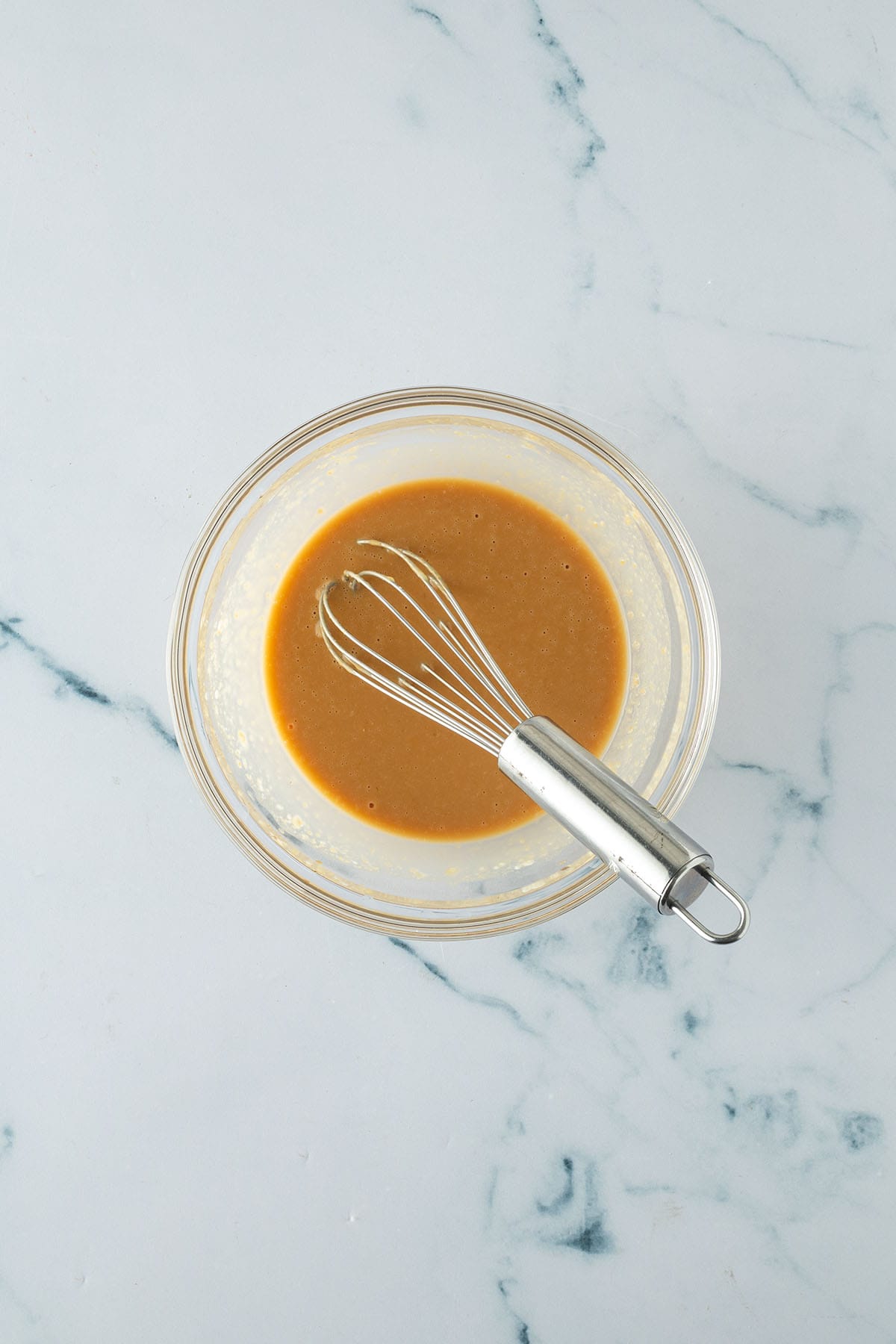 Kleine Glassch&uuml;ssel mit einer glatten Miso-Marinade, die mit einem Schneebesen auf einer hellen Arbeitsfl&auml;che verr&uuml;hrt wird.