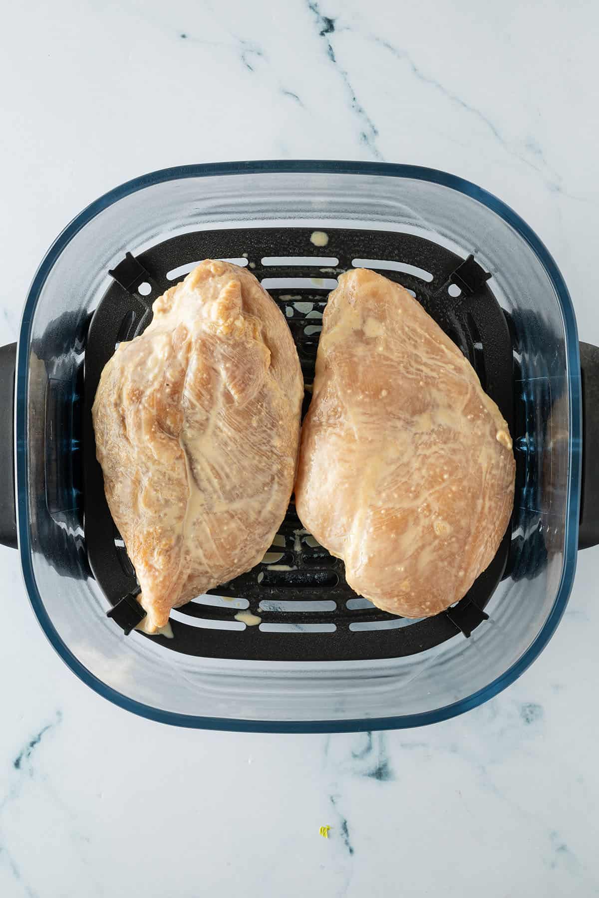 Marinierte H&auml;hnchenbrustfilets in einem Airfryer-Korb vor dem Garen.