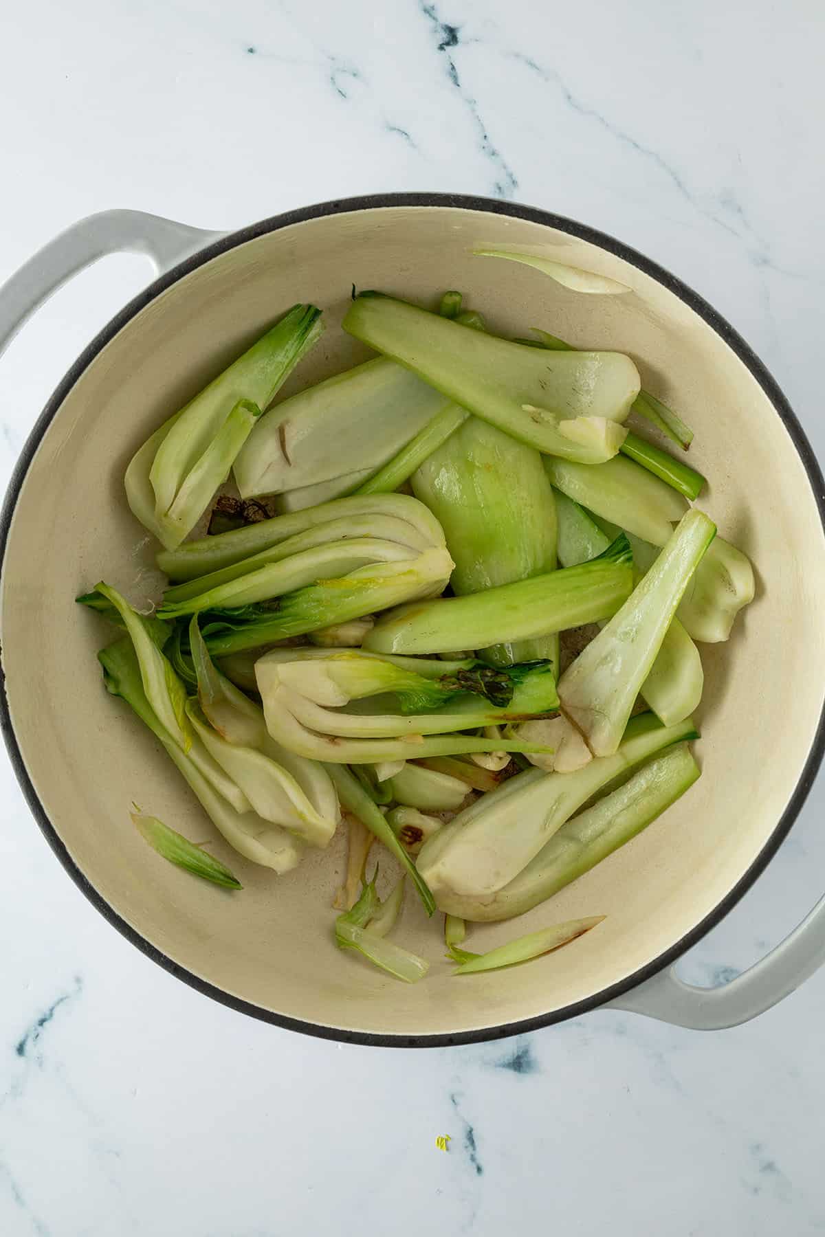 Pak Choi St&uuml;cke mit einer Knoblauchzehe und Fr&uuml;hlingszwiebeln in einem Topf beim Anbraten.