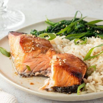 Zart gegarter Miso Lachs serviert mit Reis und gr&uuml;nem Blattgem&uuml;se auf einem Teller.