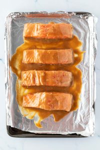 Vier mit Miso marinierte Lachsfilets auf ein mit Alufolie ausgelegtes Blech vor dem R&ouml;sten im Ofen.