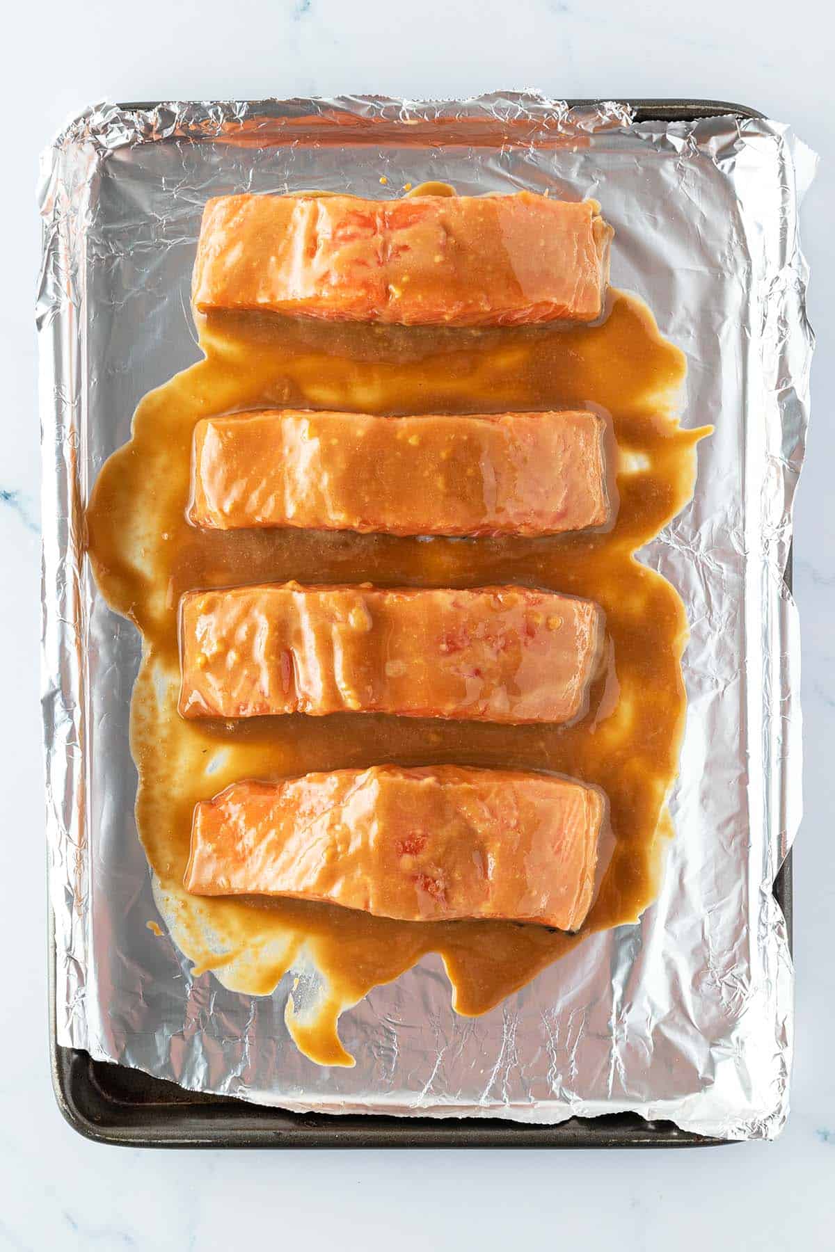 Vier mit Miso marinierte Lachsfilets auf ein mit Alufolie ausgelegtes Blech vor dem R&ouml;sten im Ofen.