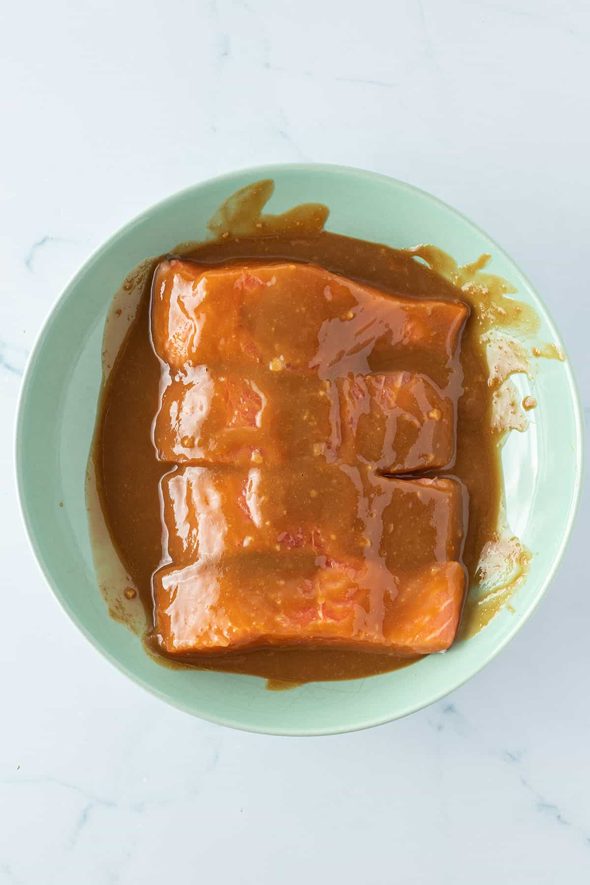 Vier rohe Lachsfilets in einem Teller, die mit der Miso-Marinade bedeckt sind.