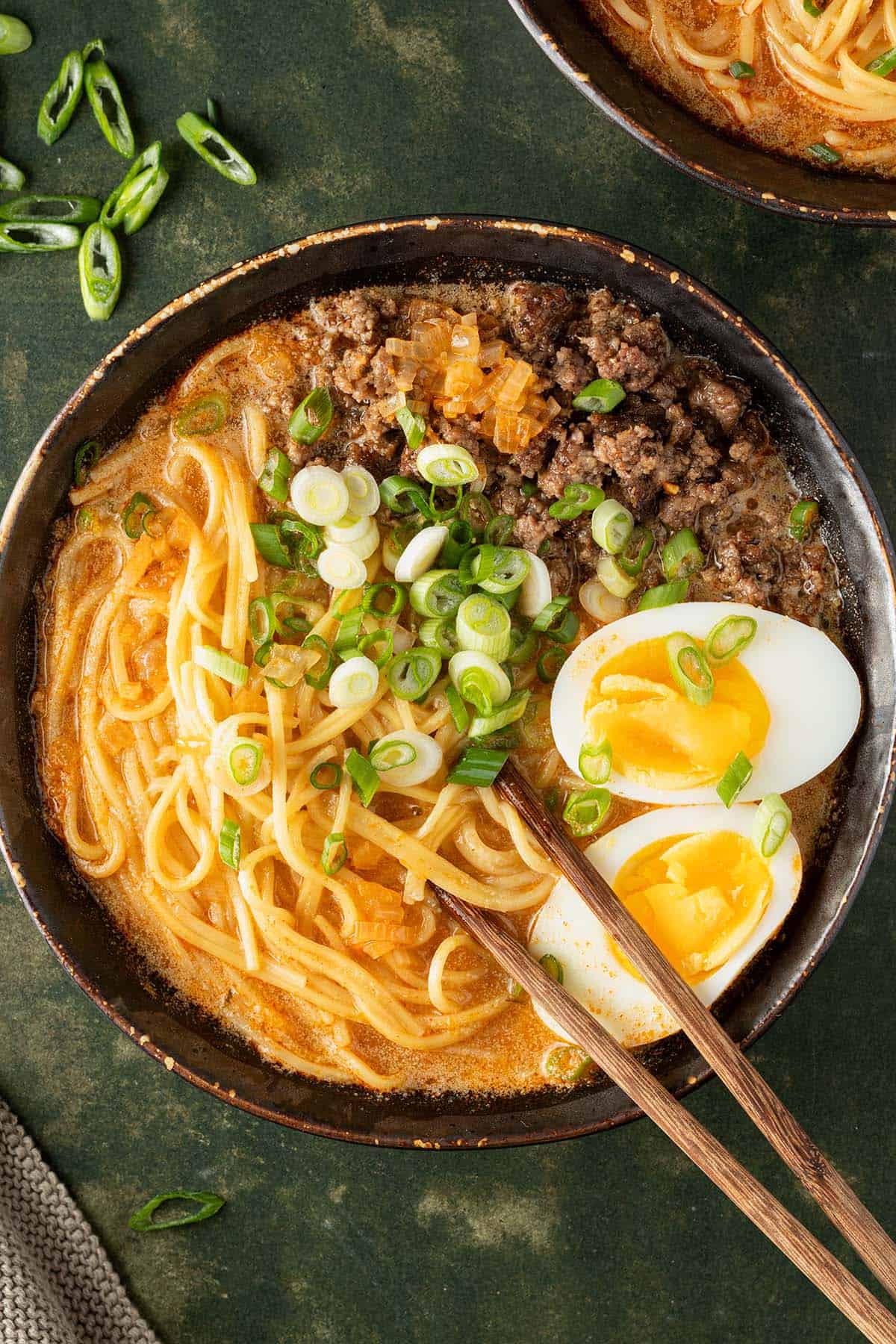 Eine Sch&uuml;ssel Miso Ramen mit Eiern, Fr&uuml;hlingszwiebeln und Hackfleisch auf einem dunkelgr&uuml;nen Untergrund.