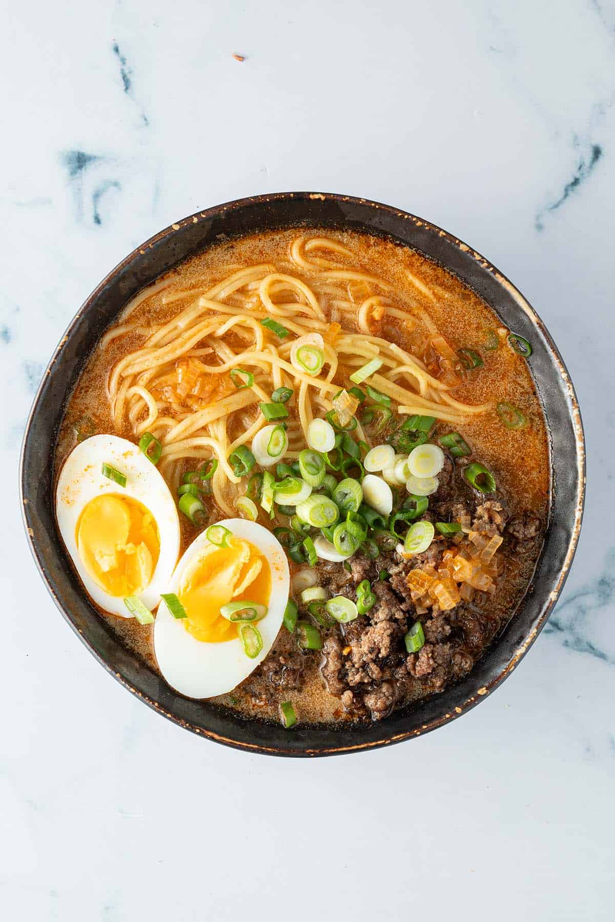 Eine Sch&uuml;ssel Miso Ramen mit d&uuml;nnen Ramennudeln, einem wachsweich gekochten Ei, Fr&uuml;hlingszwiebeln und Hackfleisch.