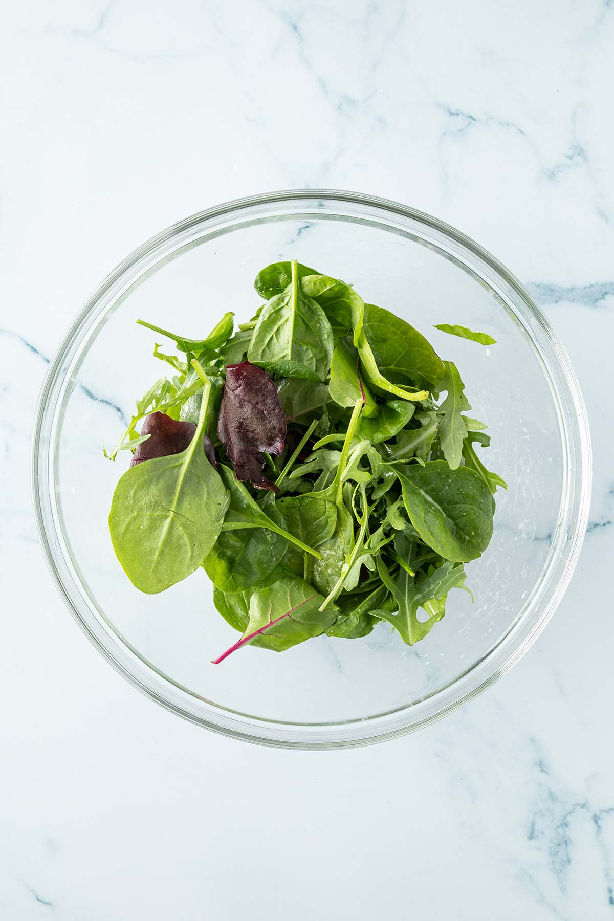 Salatbl&auml;tter in einer gro&szlig;en Glassch&uuml;ssel mit Dressing vermischt.