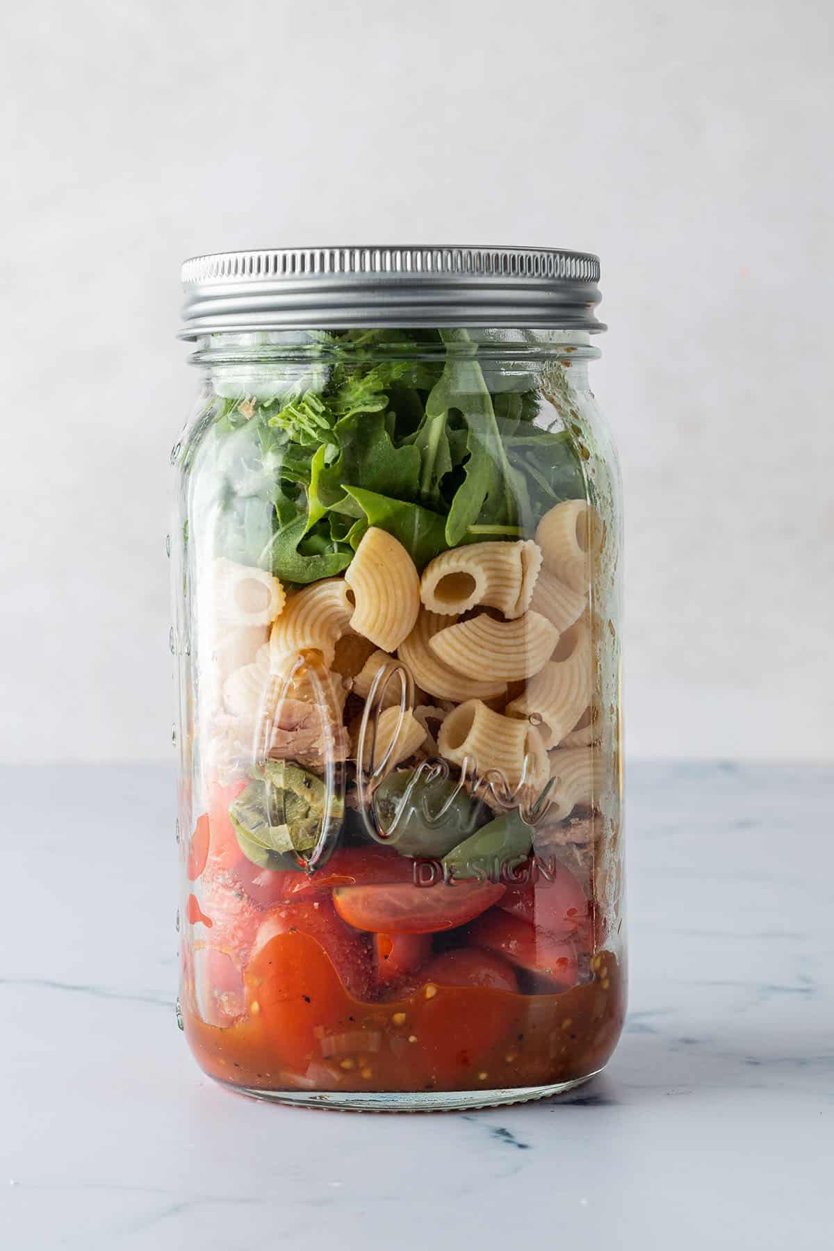In ein gro&szlig;es Glas geschichteter, italienischer Nudelsalat.